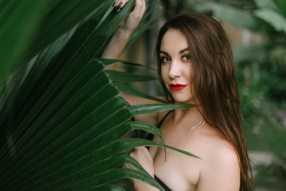 a woman with red lipstick standing next to a palm leaf