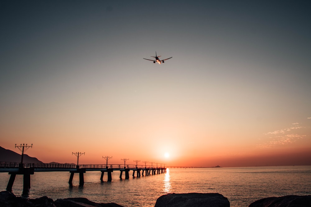 ein Flugzeug, das bei Sonnenuntergang über ein Gewässer fliegt