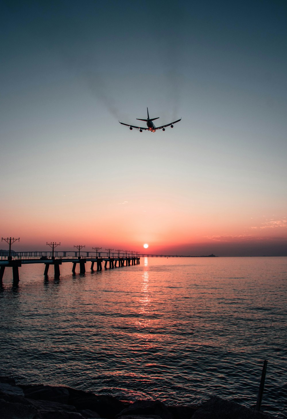 ein Flugzeug, das bei Sonnenuntergang über ein Gewässer fliegt
