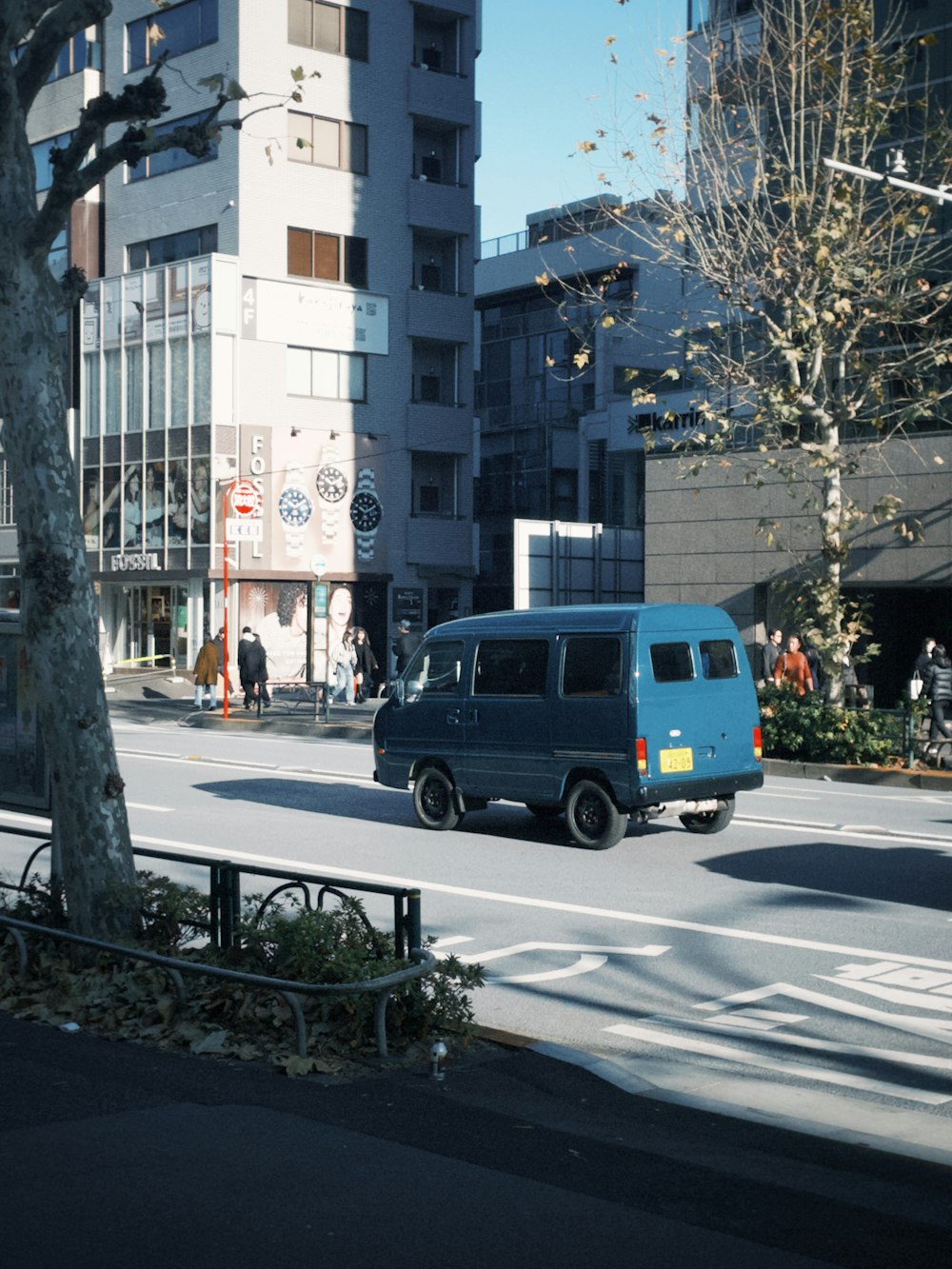 a blue van driving down a street next to tall buildings