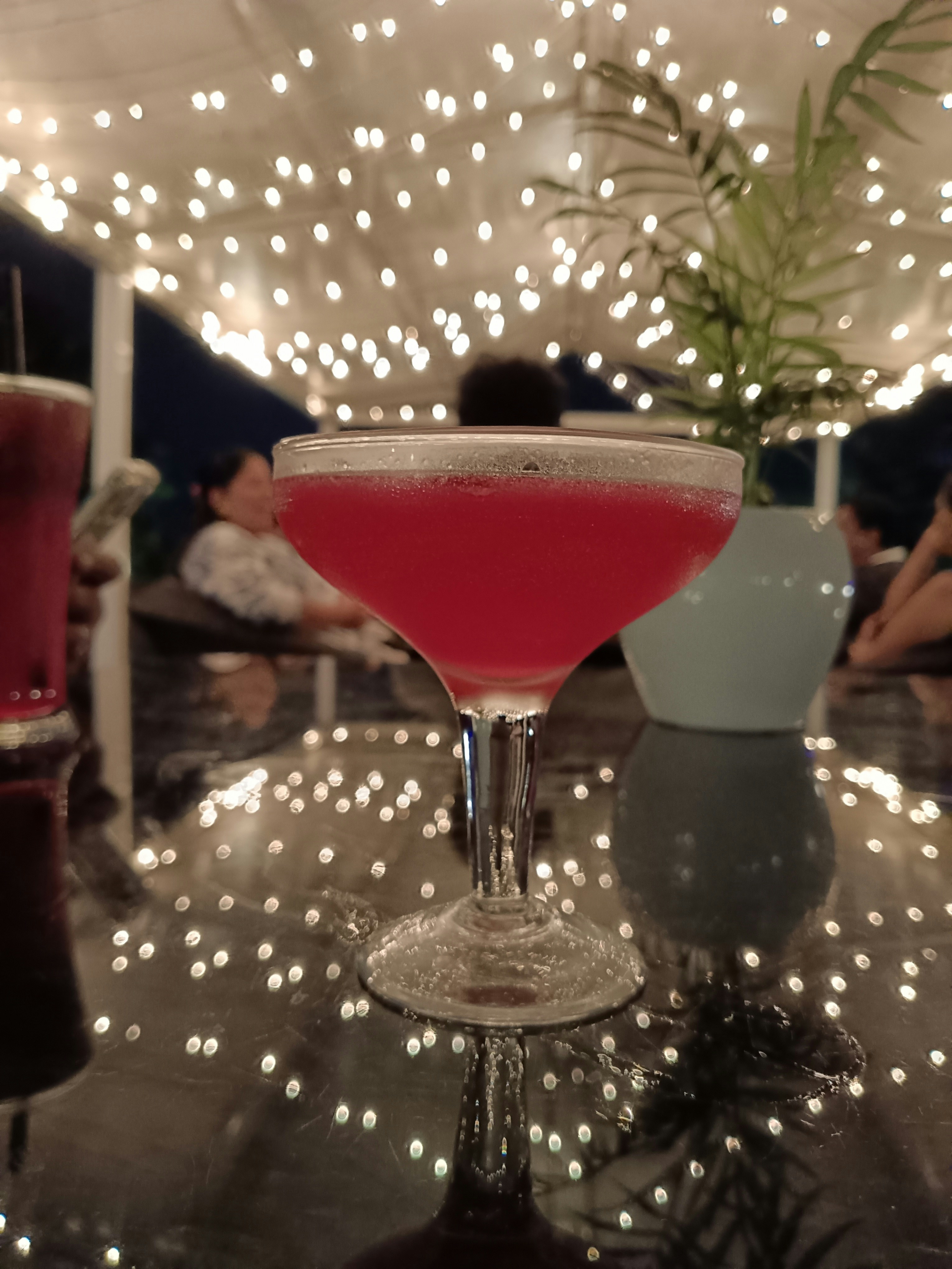 Rose-pink cocktail in coupe glass with edible flower garnish, soft amber bokeh background