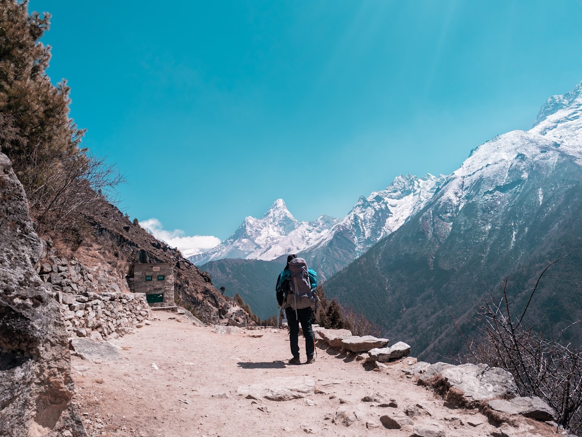 Solo trekker with backpack walking up mountain trail toward Everest Base Camp Nepal