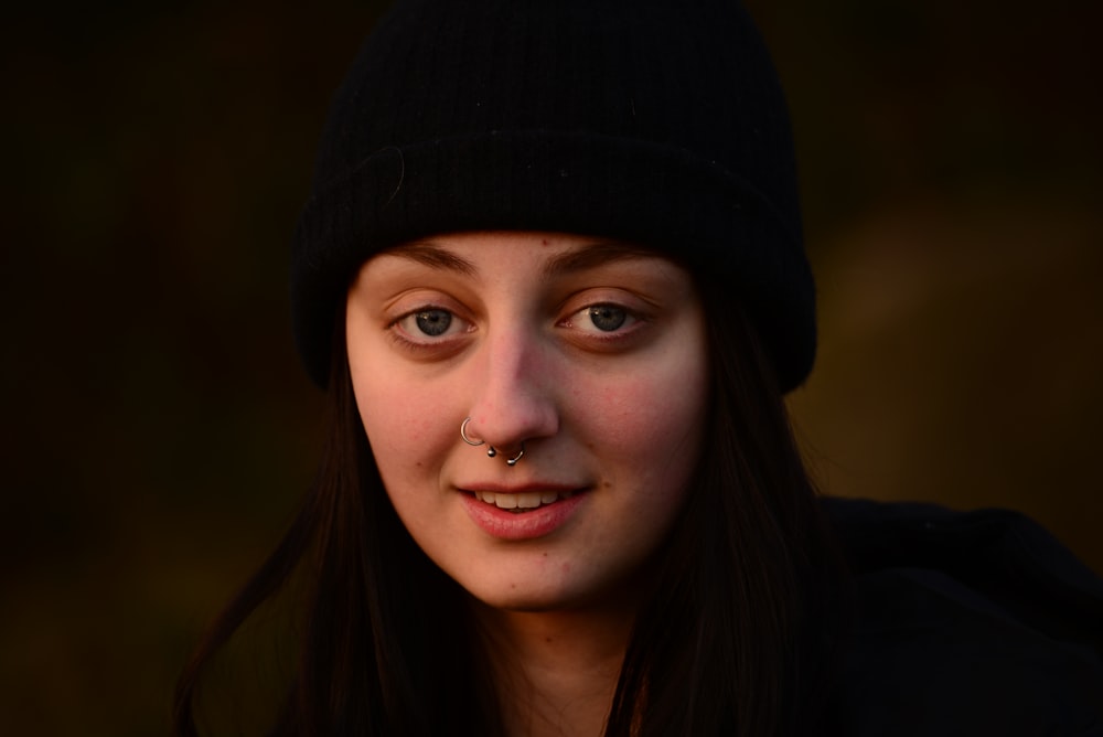 a woman with a nose piercing wearing a black hat