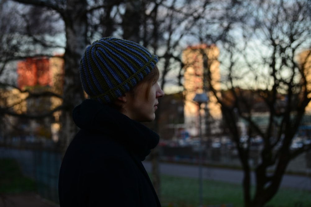 a man wearing a beanie standing in front of a tree