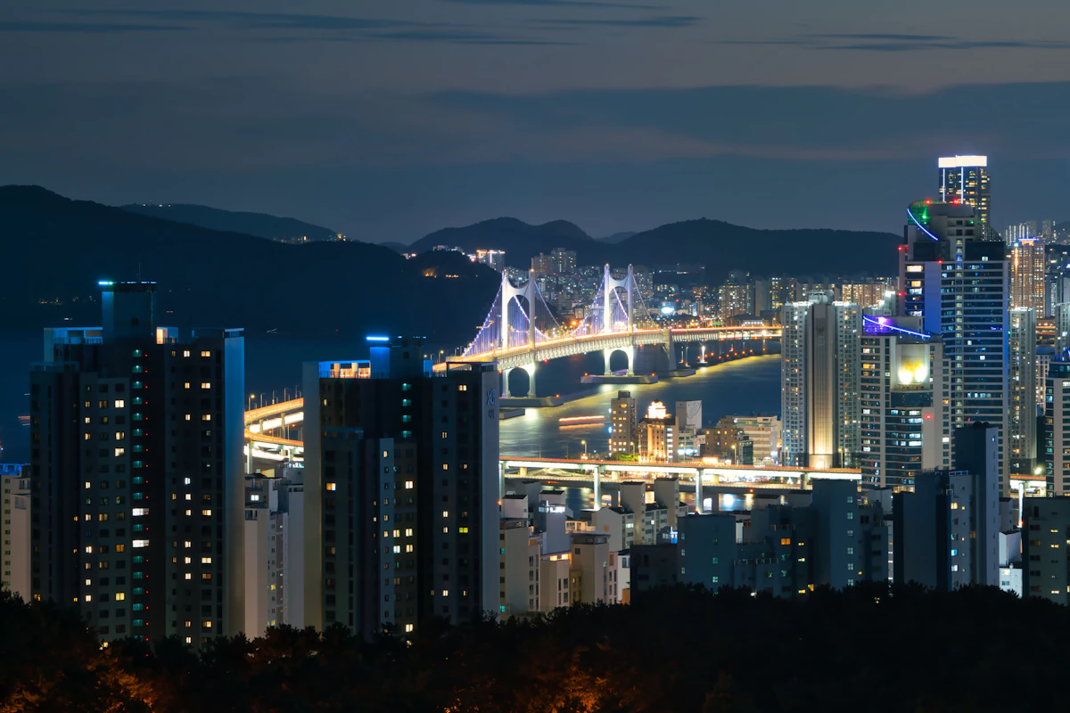 The lit Gwangan Bridge and high rise towers along the Busan coastline at night