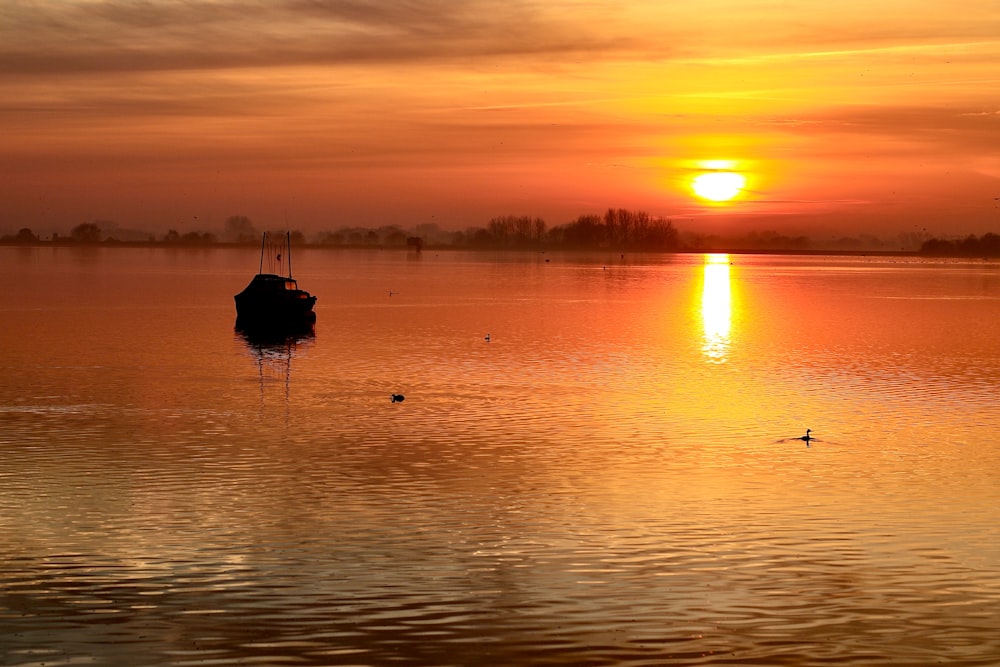 a boat floating on top of a lake at sunset