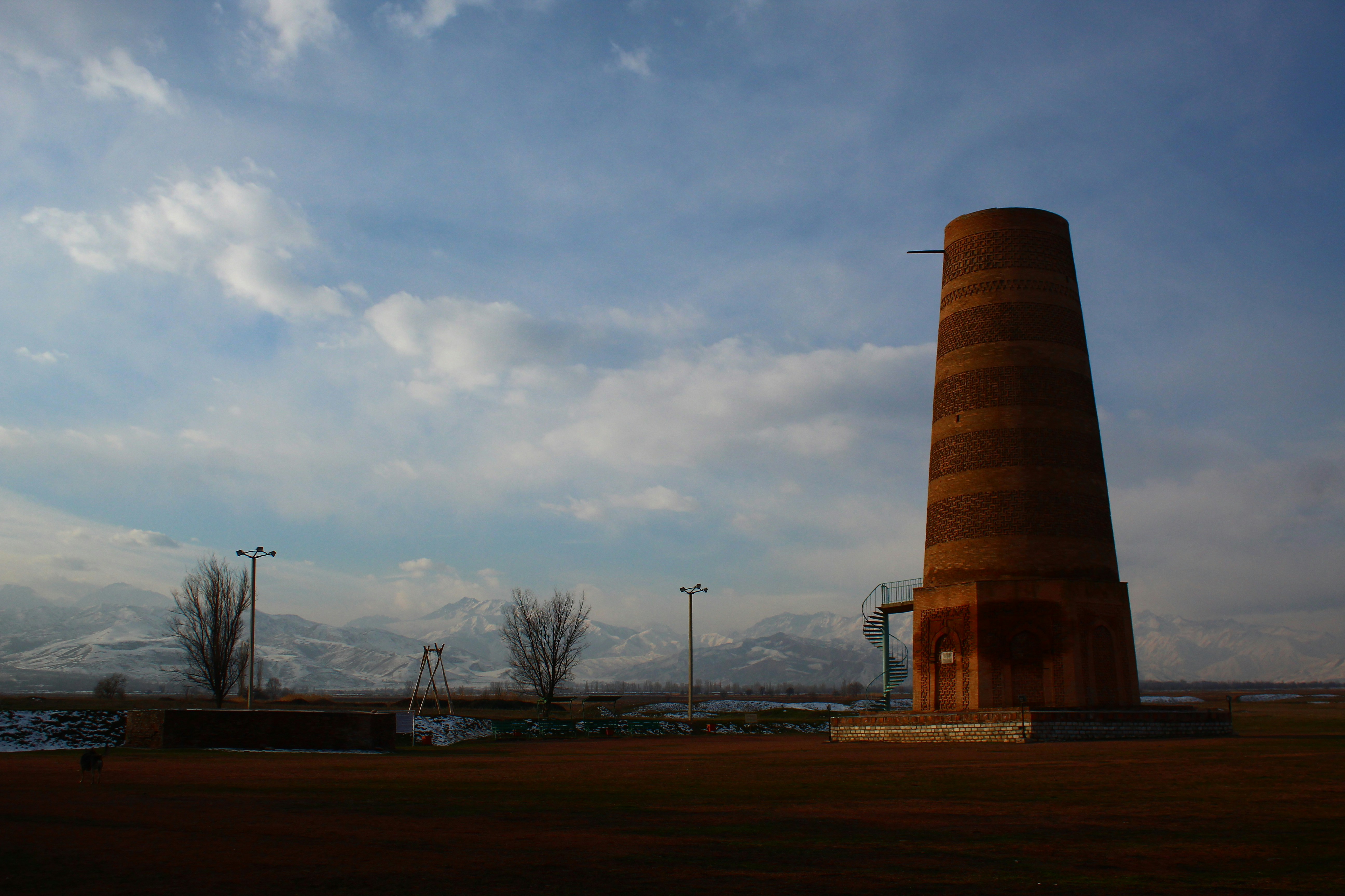 a tall tower sitting in the middle of a field, Tien Shan Mountains and Burana Tower from Balasagun (capital city of Kara-Khanid Khanate)