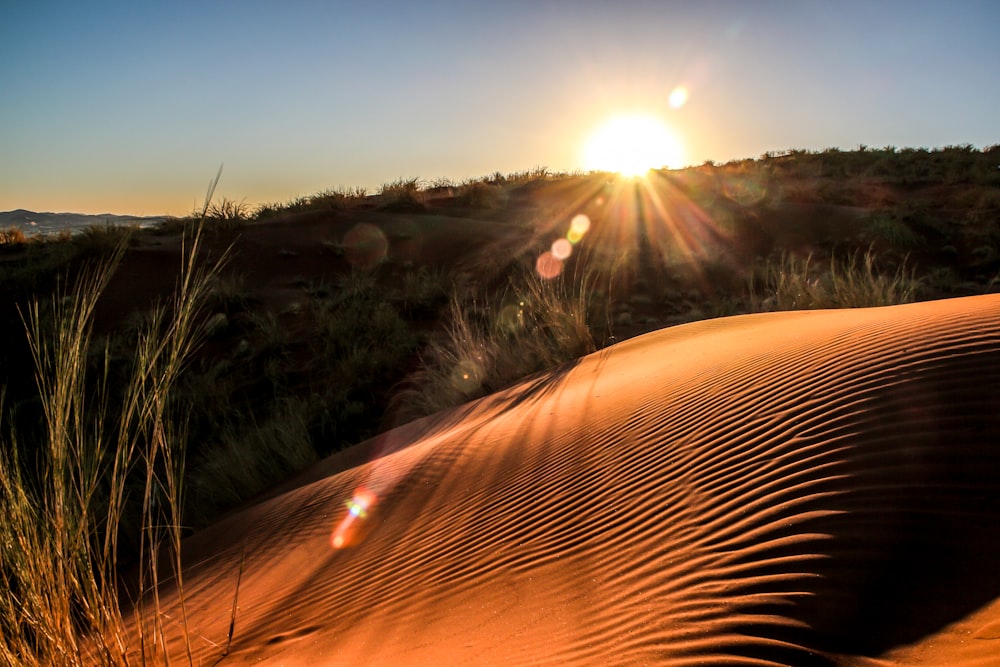 the sun is setting over a sand dune