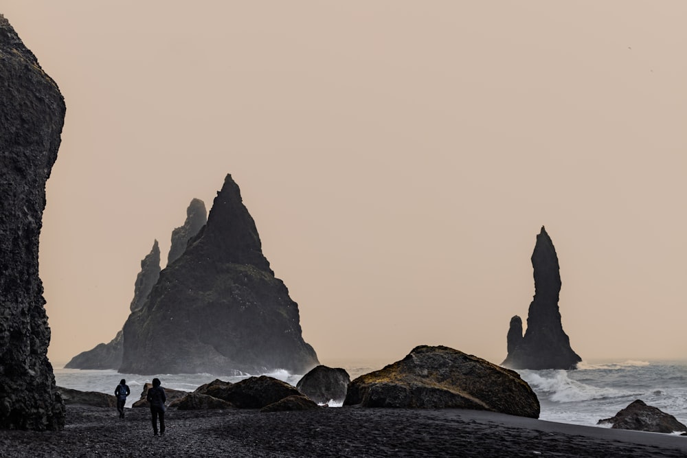 two people walking on a beach near rocks