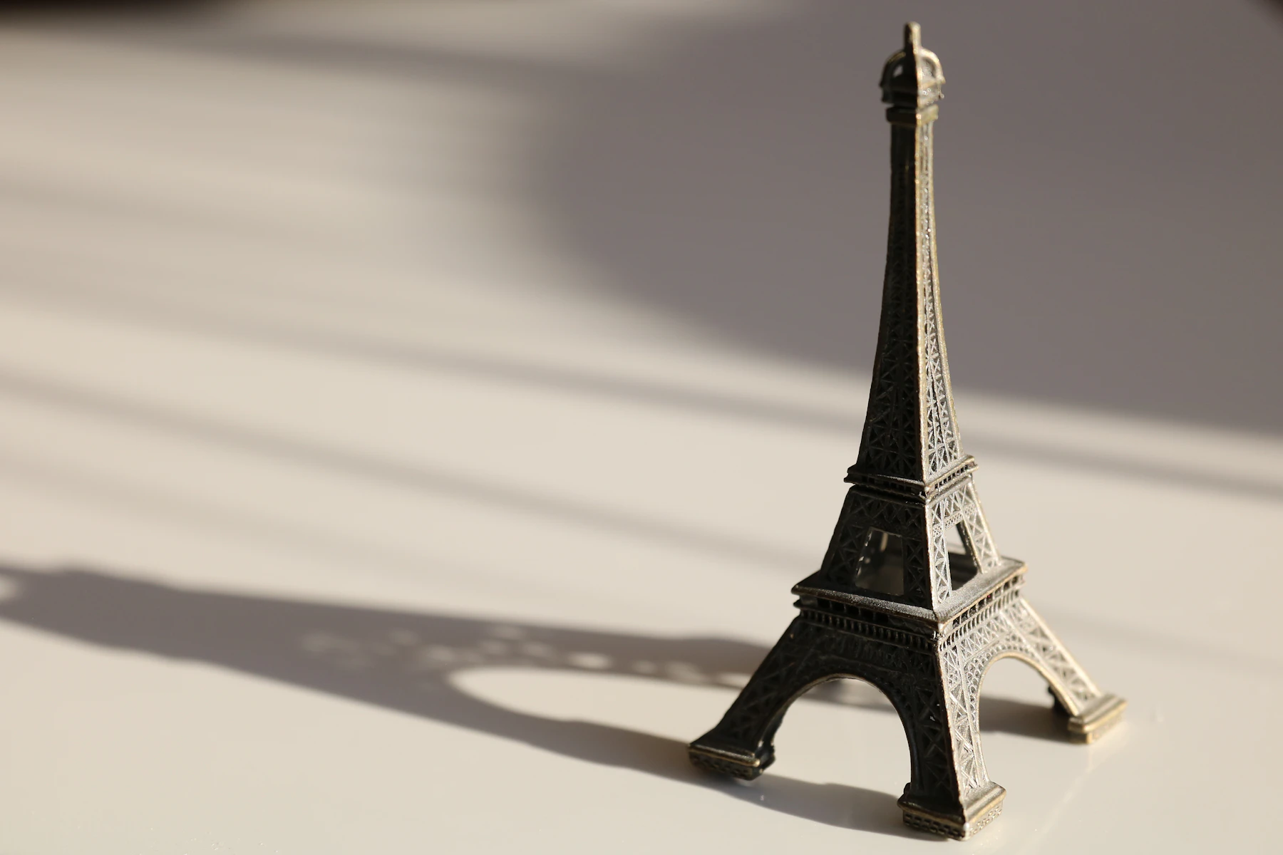 A small dark metal Eiffel Tower model standing on a pale table, casting a long shadow