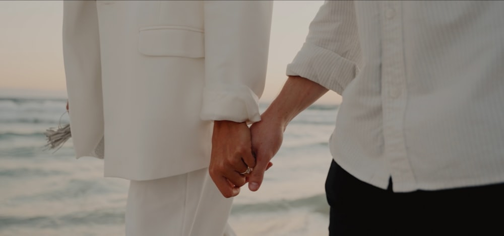 a couple holding hands while standing on a beach