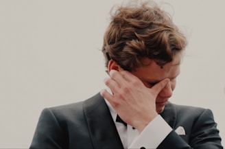 a man in a tuxedo holds his hand to his face