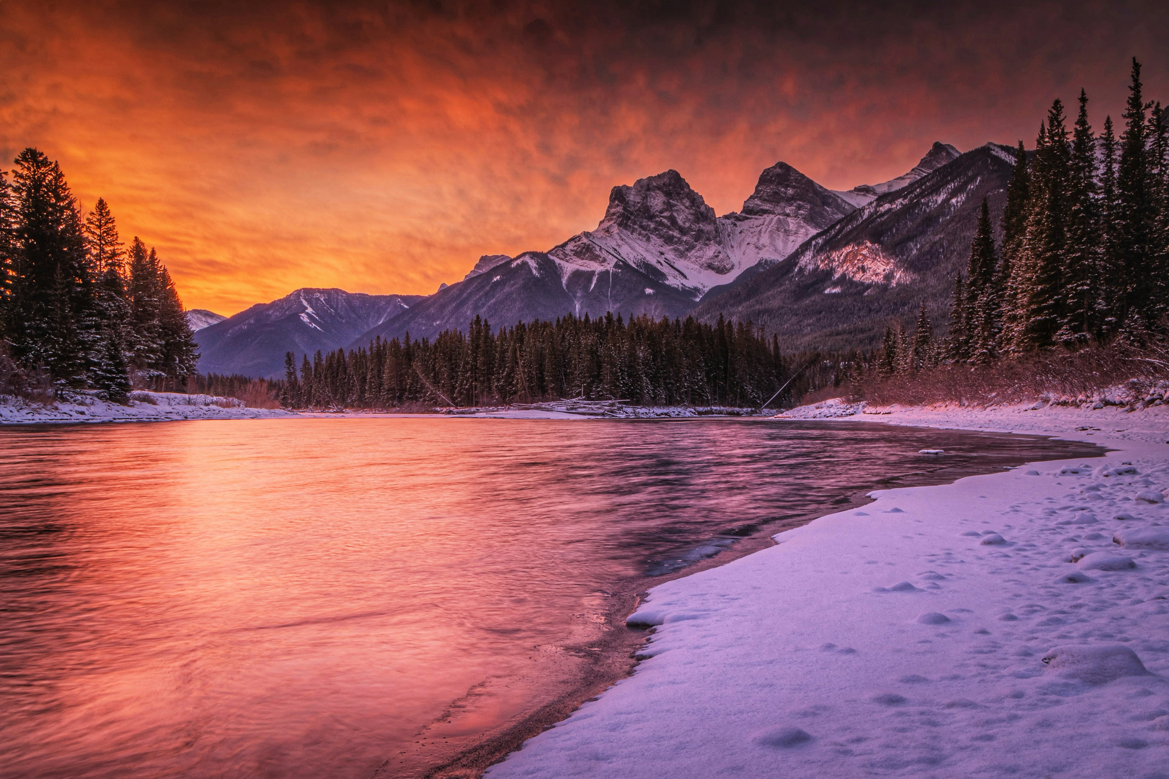 a sunset over a mountain lake with snow on the ground
