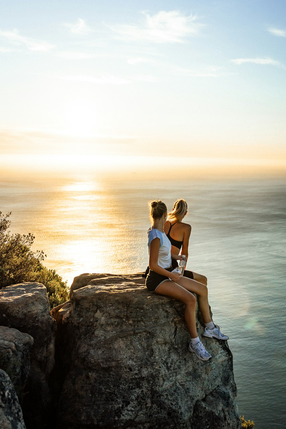 two women sitting on a rock overlooking the ocean