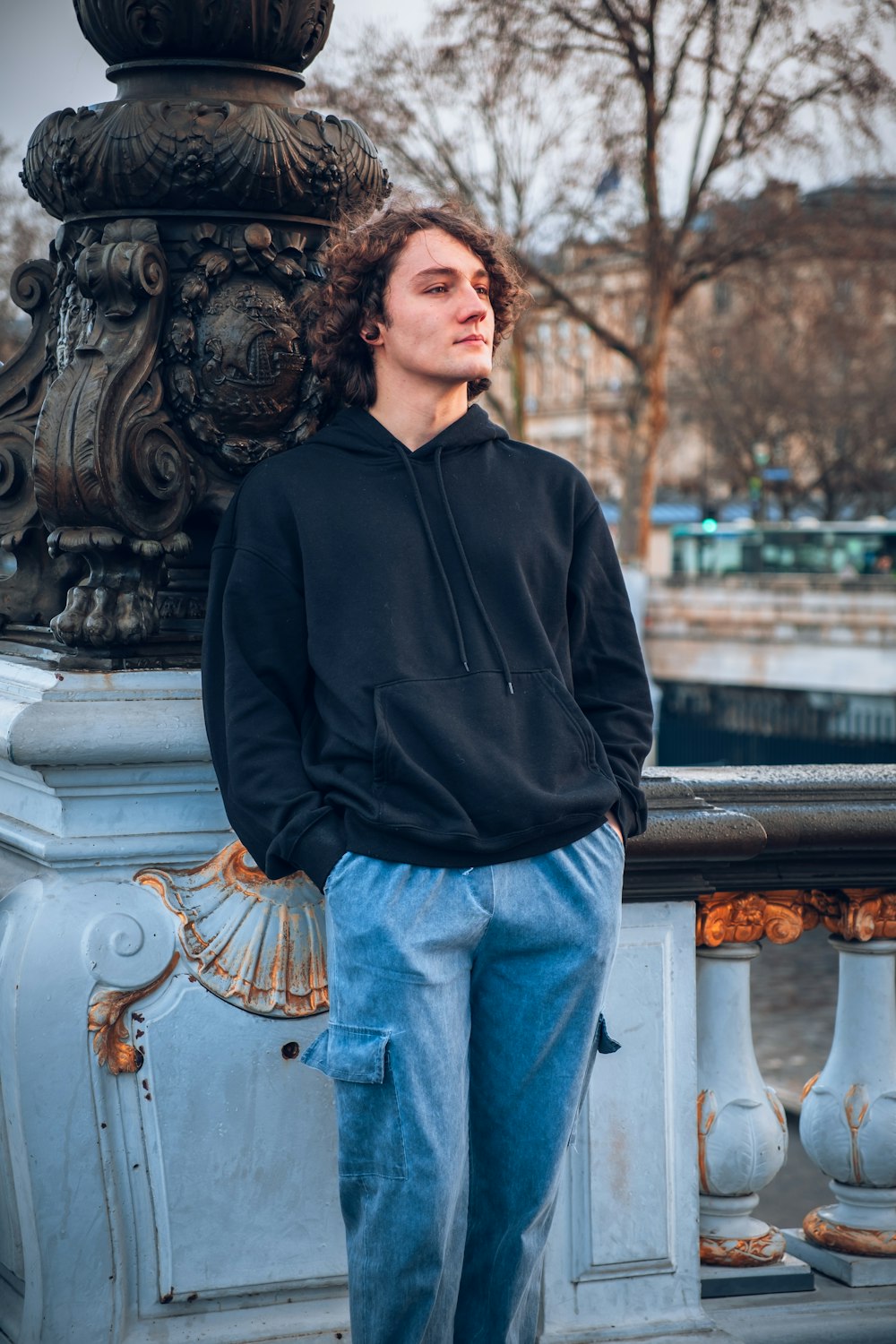 a young man leaning against a wall with his hands in his pockets