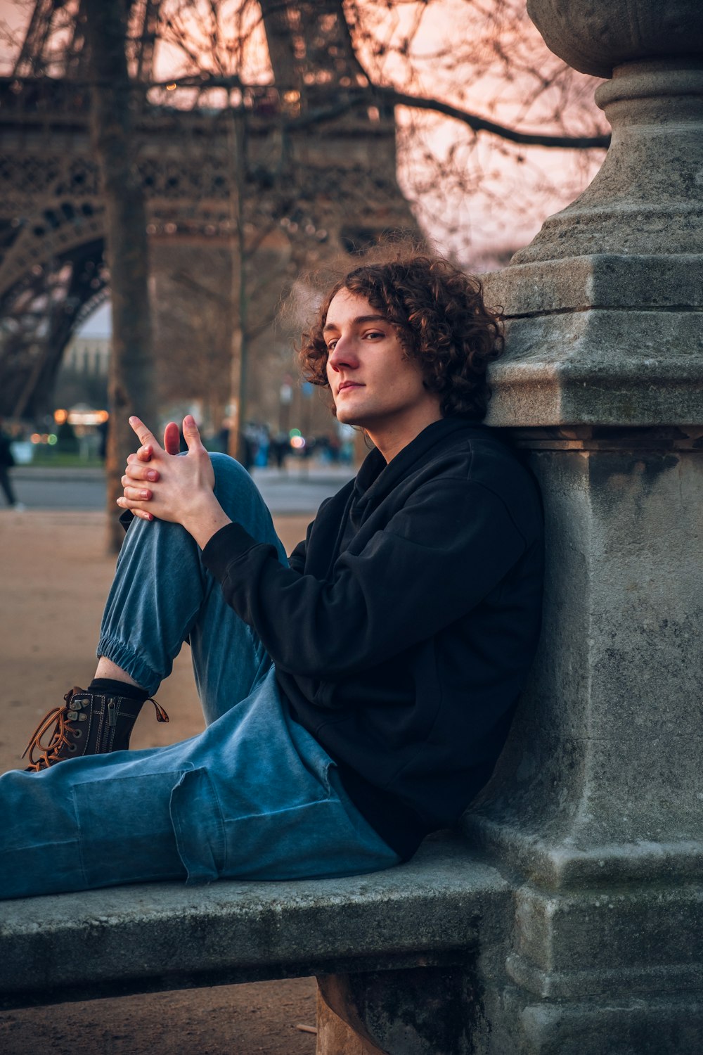 a man sitting on a stone bench in front of the eiffel tower