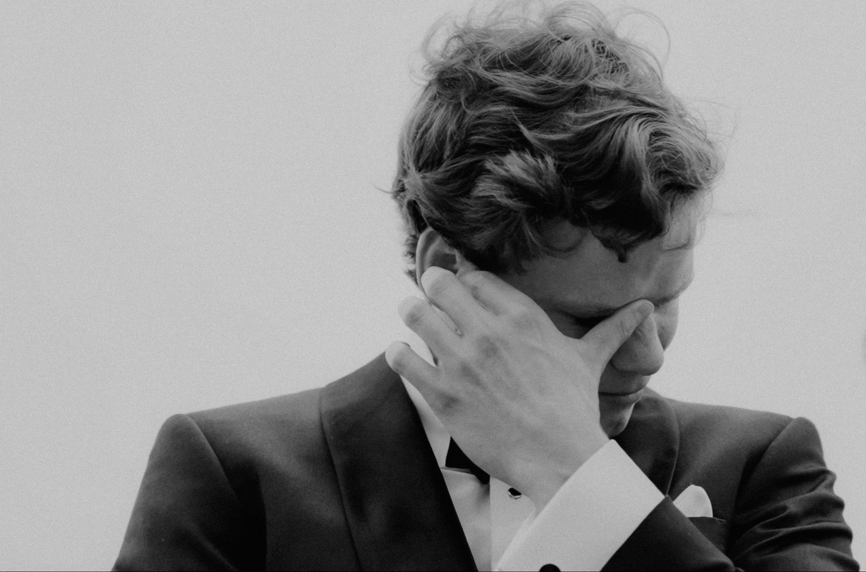 a black and white photo of a man in a suit holding his hands to his