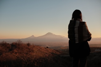 a woman standing on top of a hill looking at a mountain
