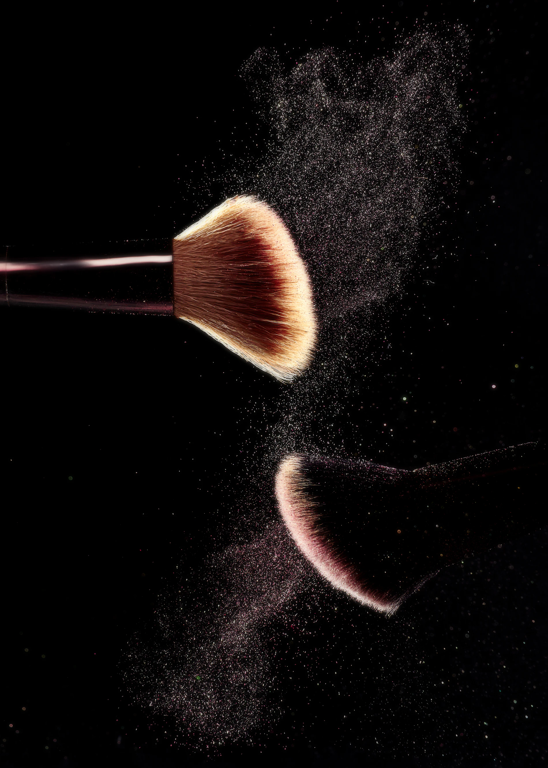 A makeup brush releasing loose powder against a dark ground
