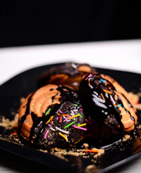 a black plate topped with chocolate covered donuts