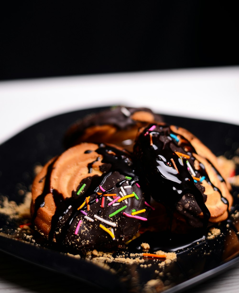 a black plate topped with chocolate covered donuts