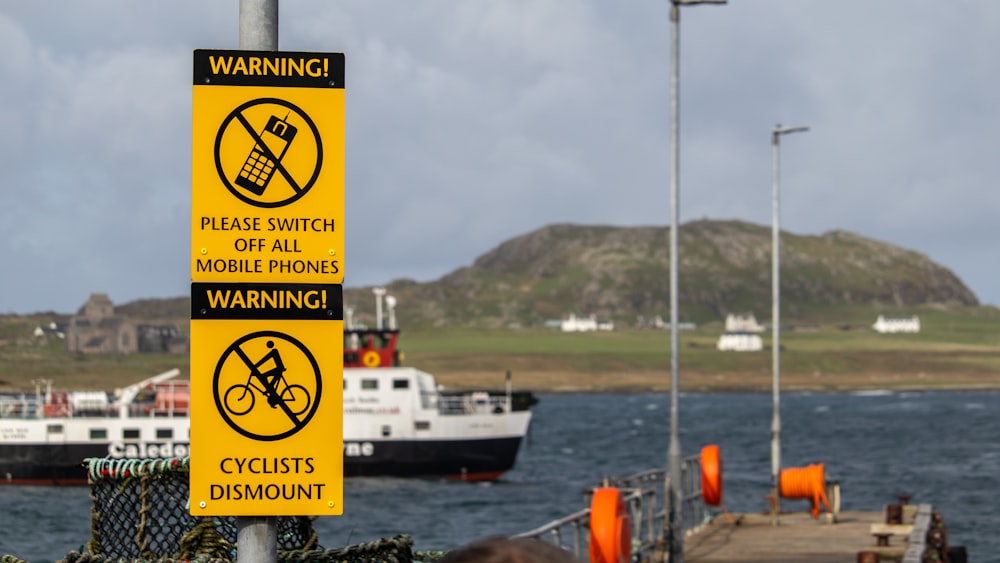 a warning sign on a pole next to a body of water