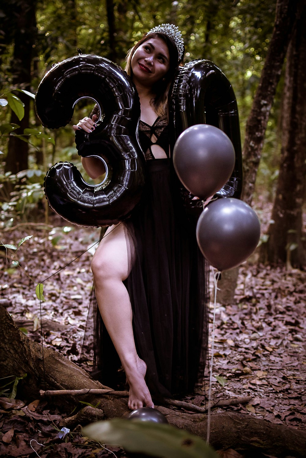 a woman in a black dress holding a number three balloon
