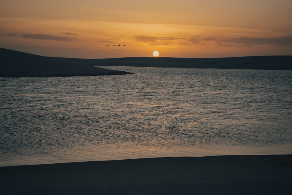 a sunset over a body of water with birds flying in the sky