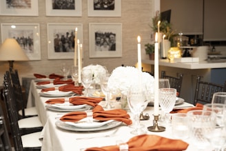 a table set for a formal dinner with orange napkins