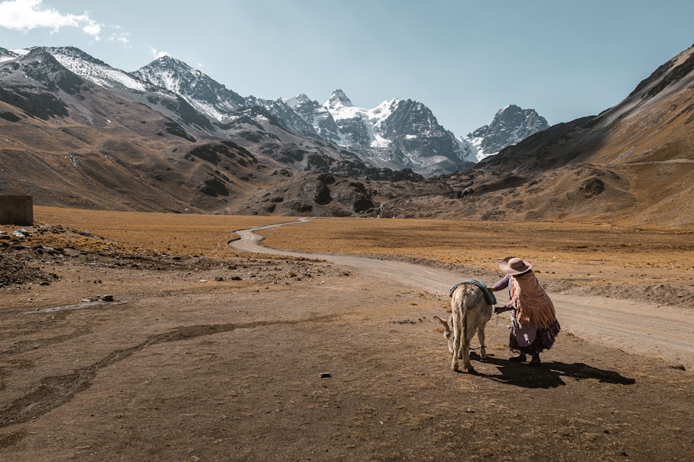 a woman leading a horse down a dirt road