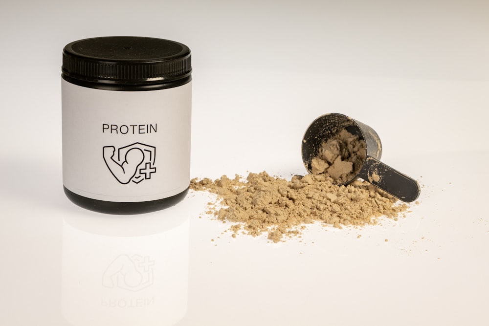 a jar of protein powder next to a scoop of protein powder