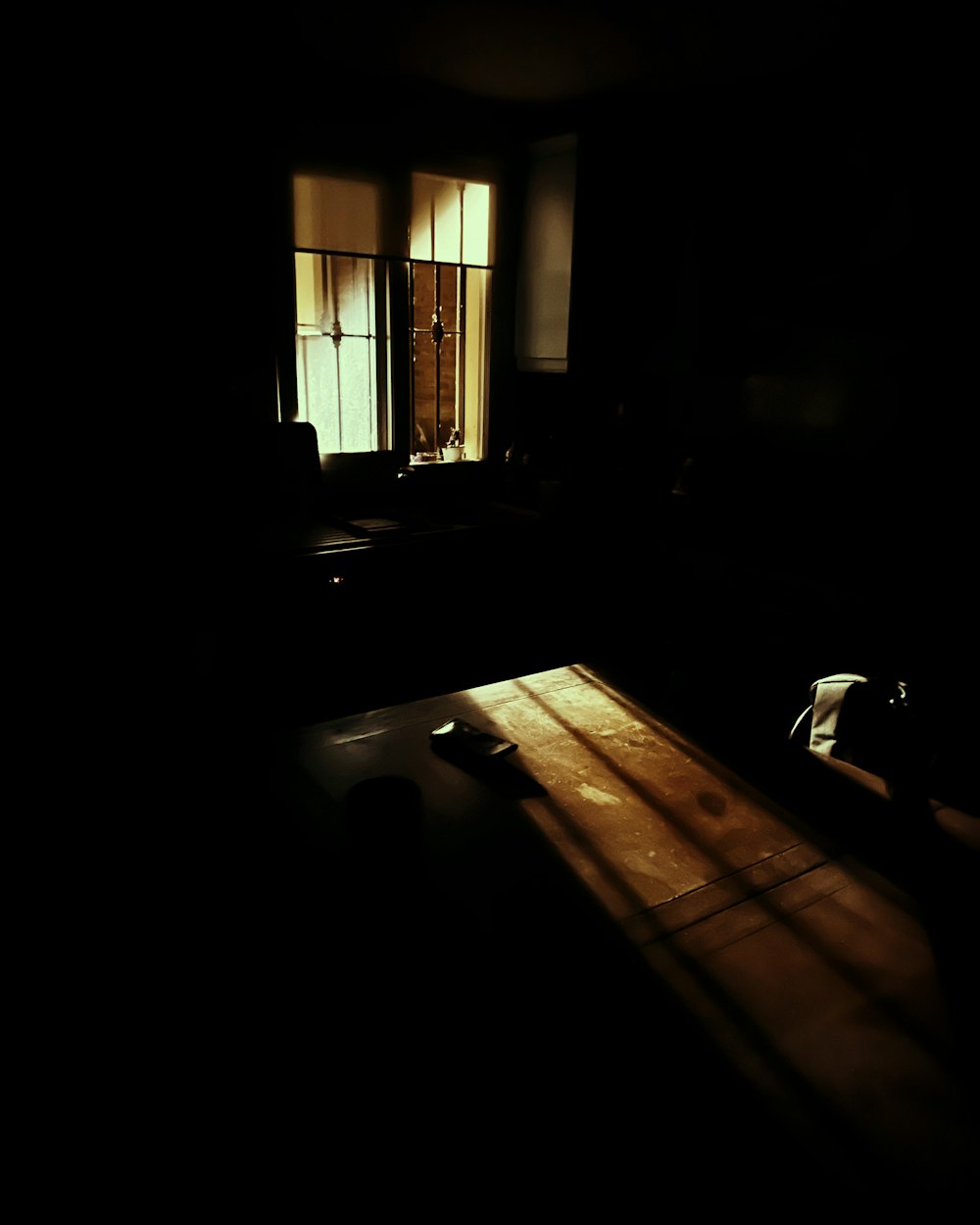 a dark room with a wooden table and two windows
