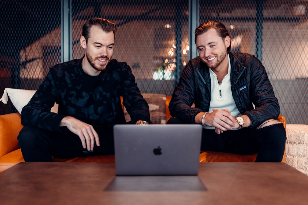 two men sitting at a table looking at a laptop