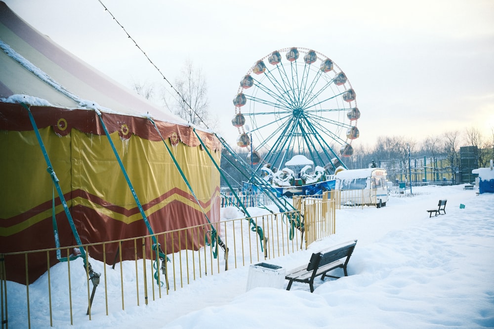 a park bench covered in snow next to a ferris wheel