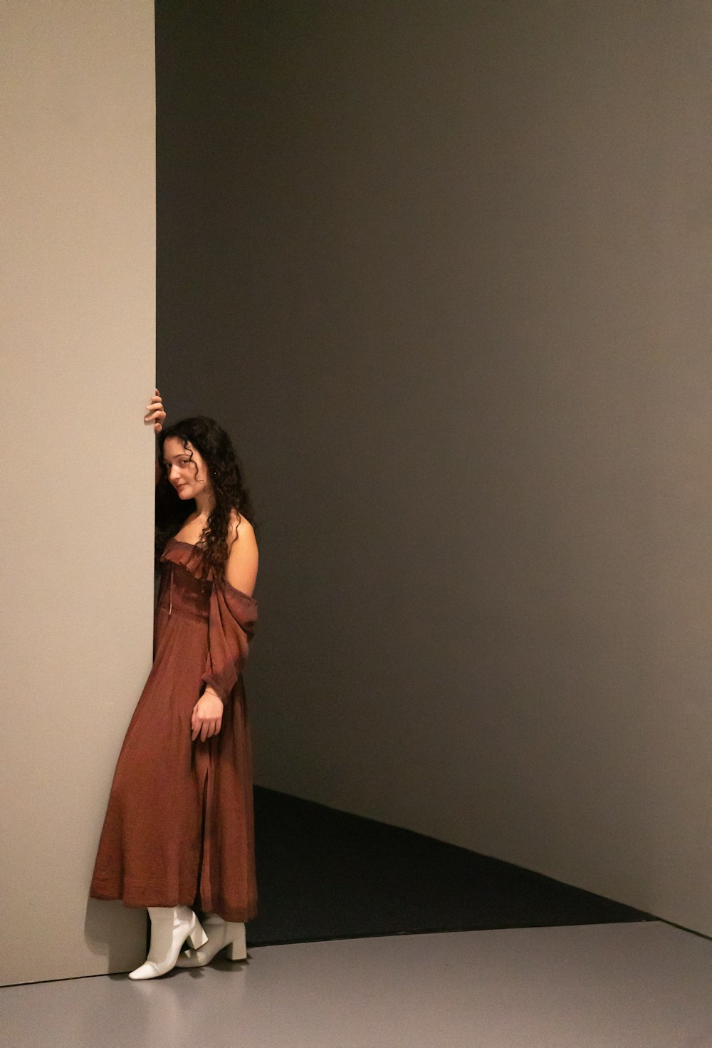 a woman in a brown dress leaning against a wall