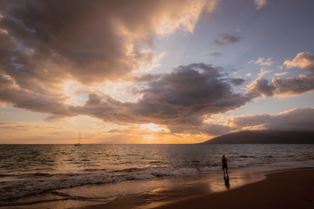 una persona in piedi su una spiaggia al tramonto