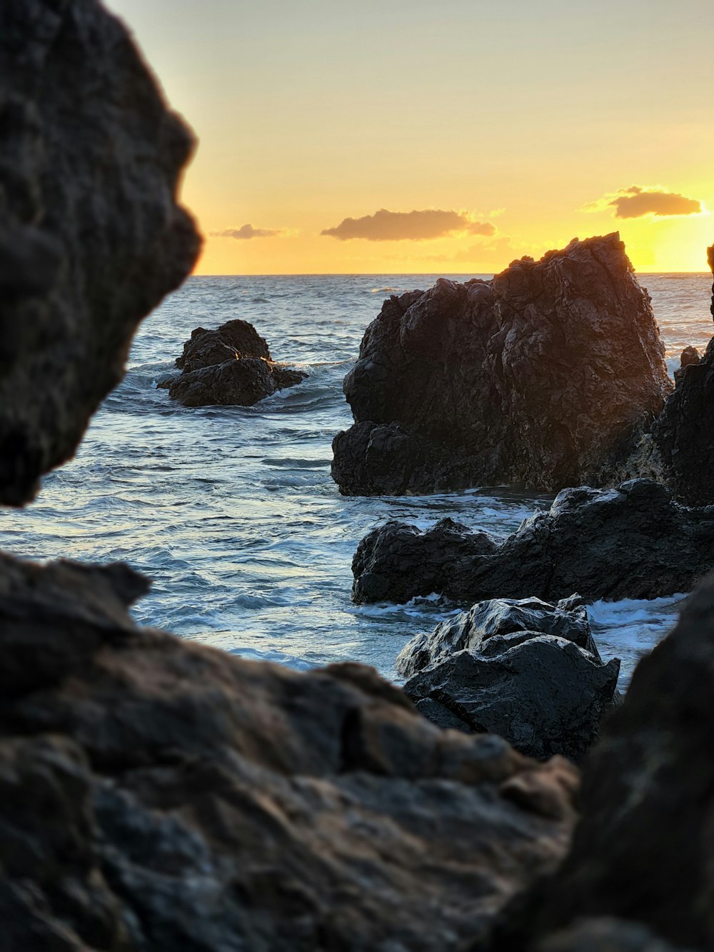 the sun is setting over the ocean and rocks