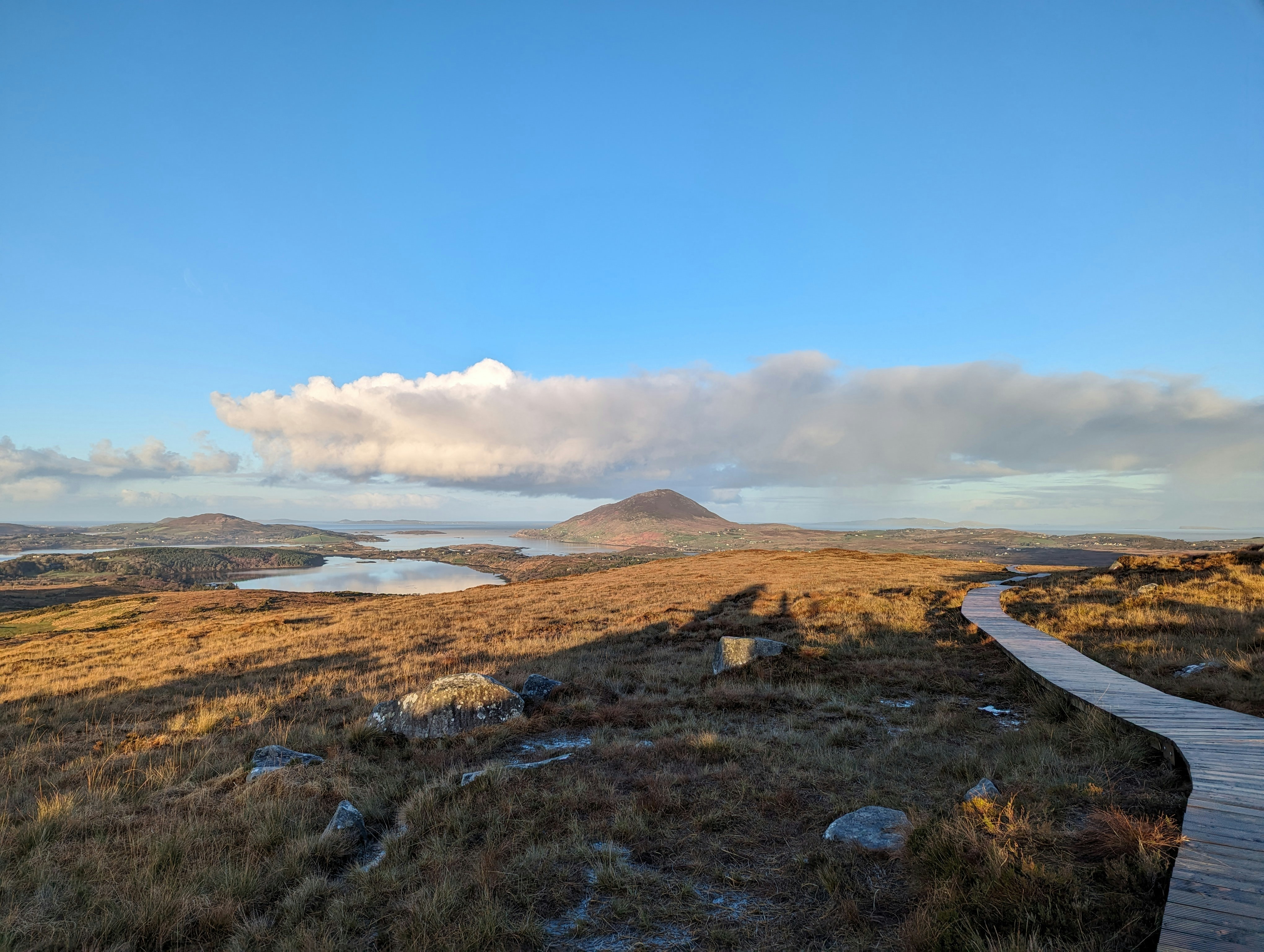 a wooden walkway in a grassy field with mountains in the background, View from Diamond Hill in Connemara National Park in Galway Ireland