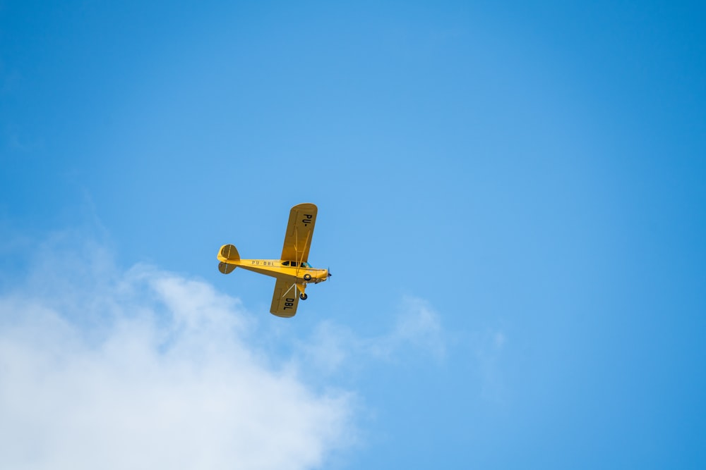 a small yellow airplane flying through a blue sky