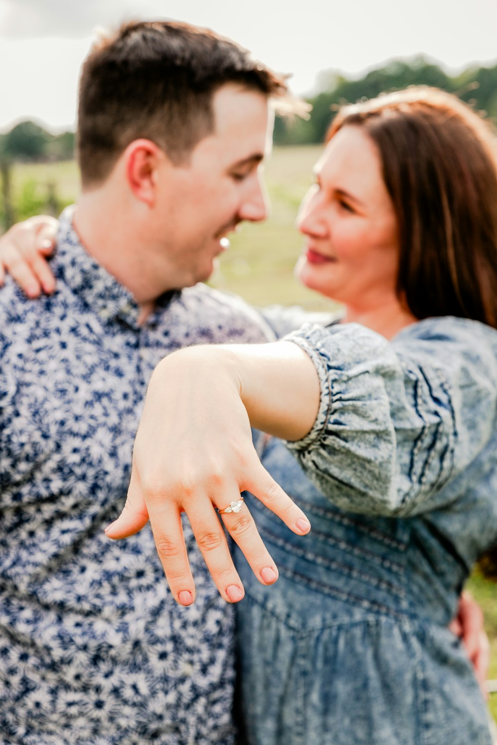 a man and a woman standing in a field with their arms around each other