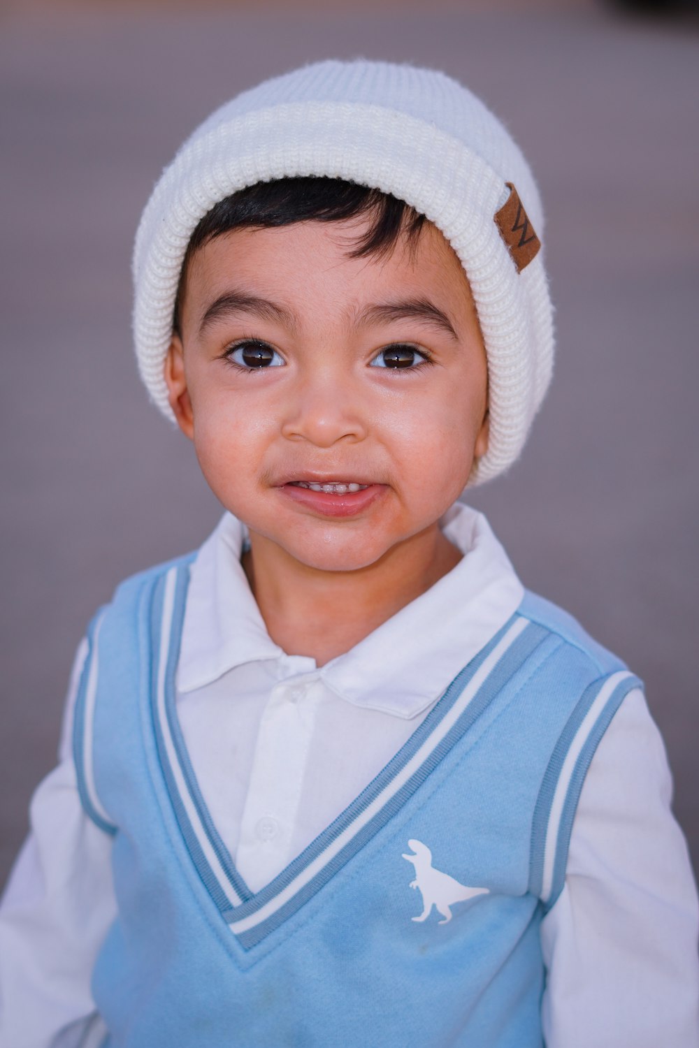 a young boy wearing a blue vest and a white hat