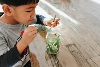 a young boy sitting at a table with a jar of water