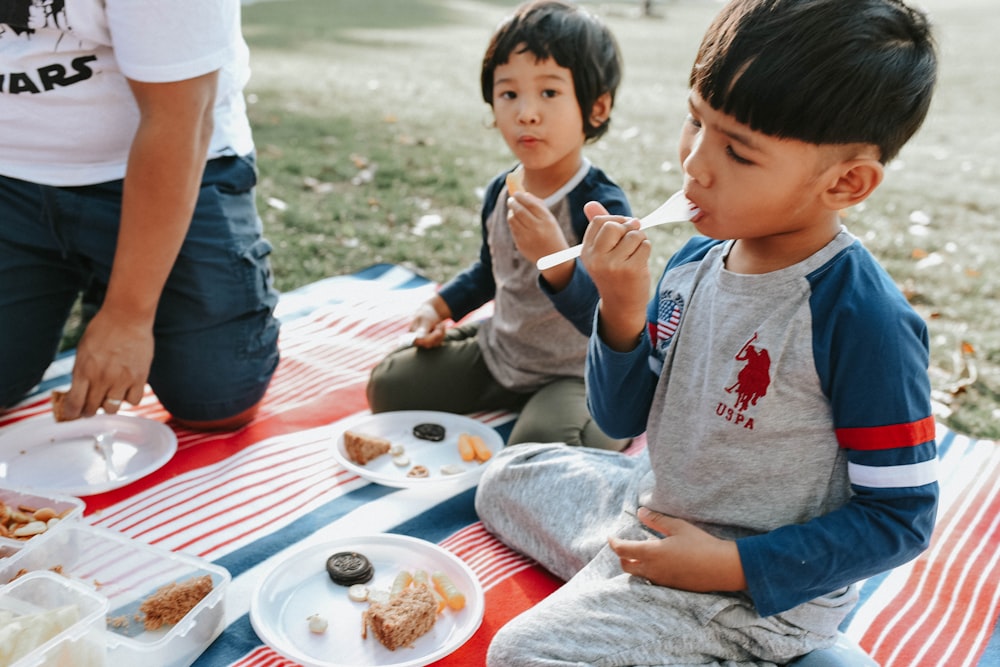 a couple of kids sitting on top of a red and white blanket