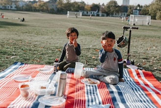two young boys sitting on a blanket eating food