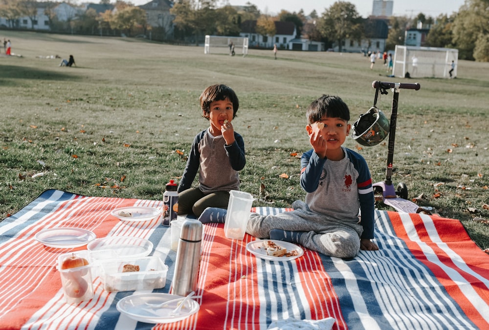 two young boys sitting on a blanket eating food