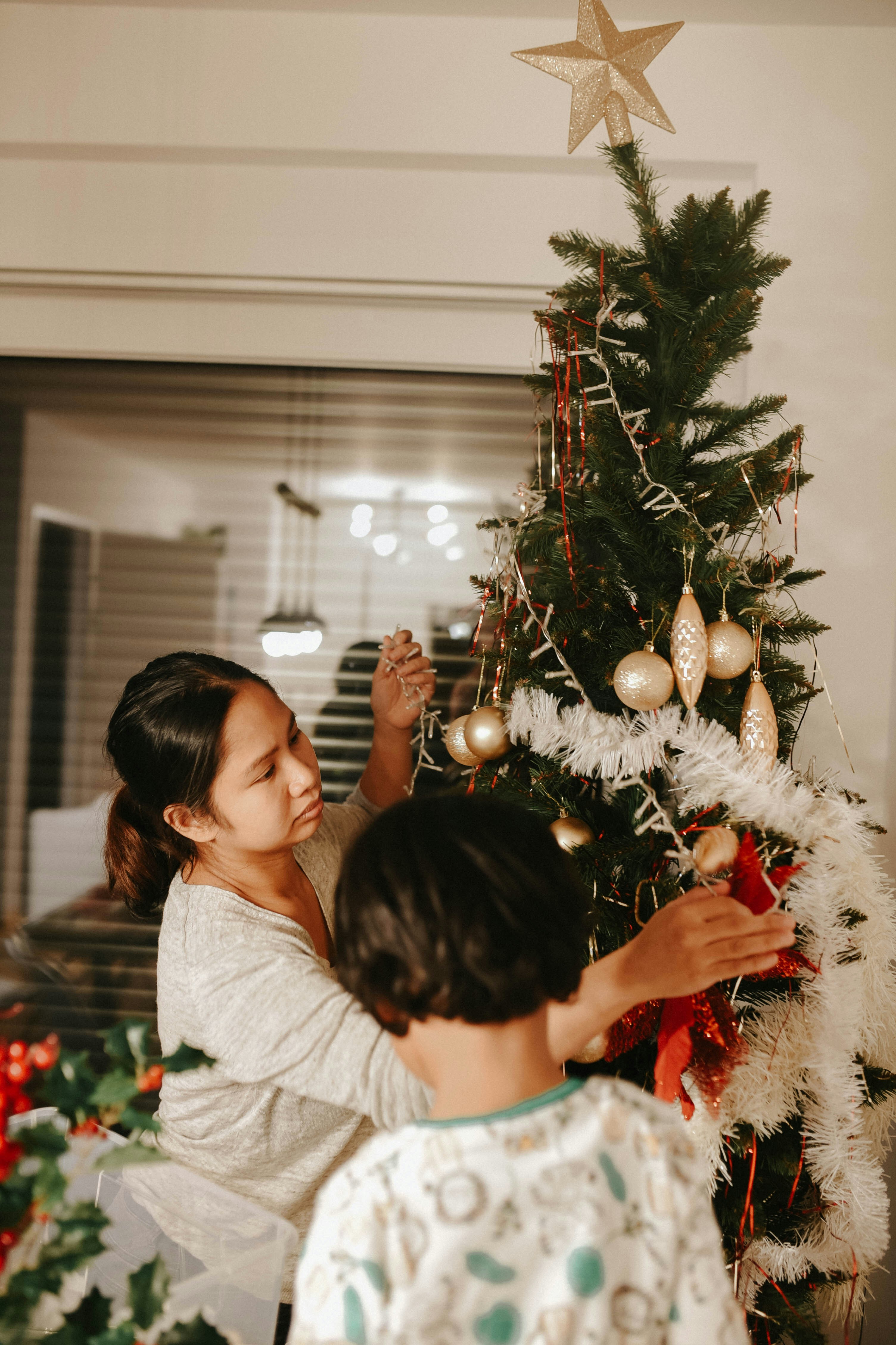 a woman and a child decorating a christmas tree