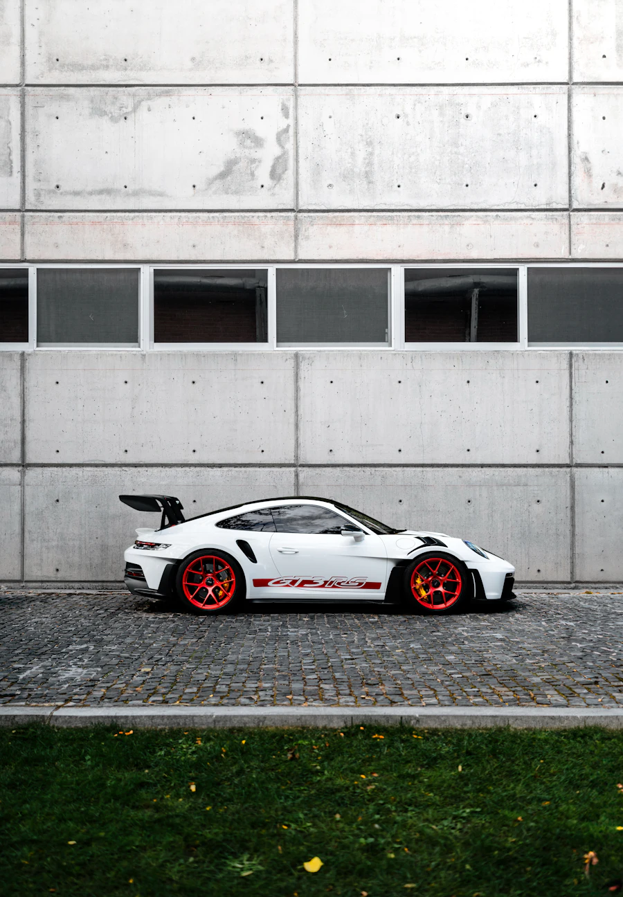 White Porsche 911 GT3 RS with red wheels parked by a concrete wall