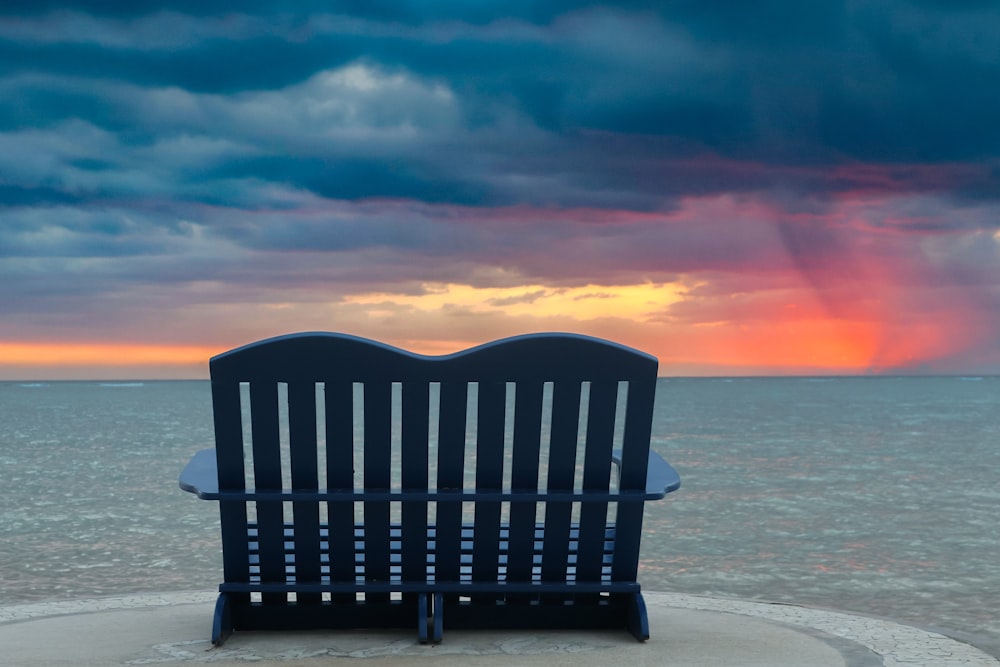 a blue bench sitting on top of a beach under a cloudy sky