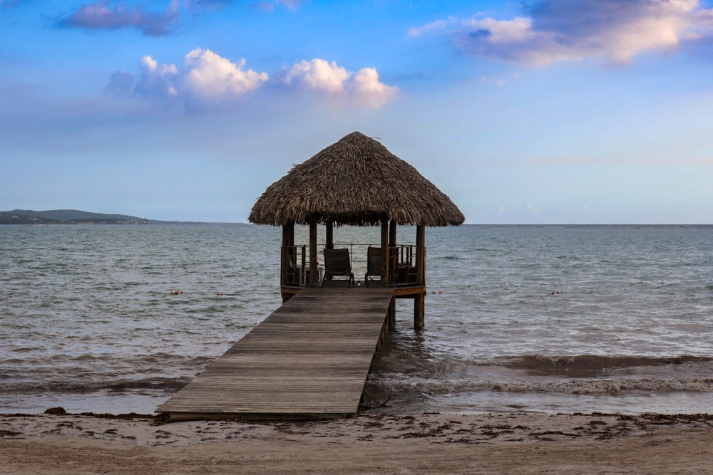 a pier with a thatched roof on a beach