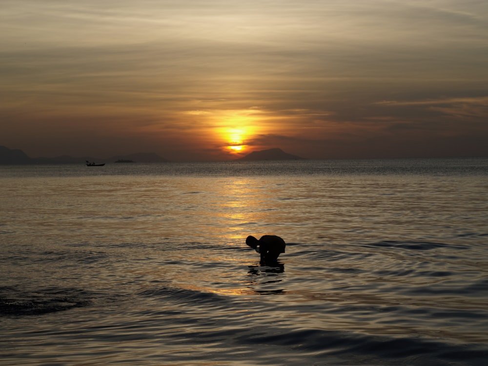 a person swimming in the ocean at sunset